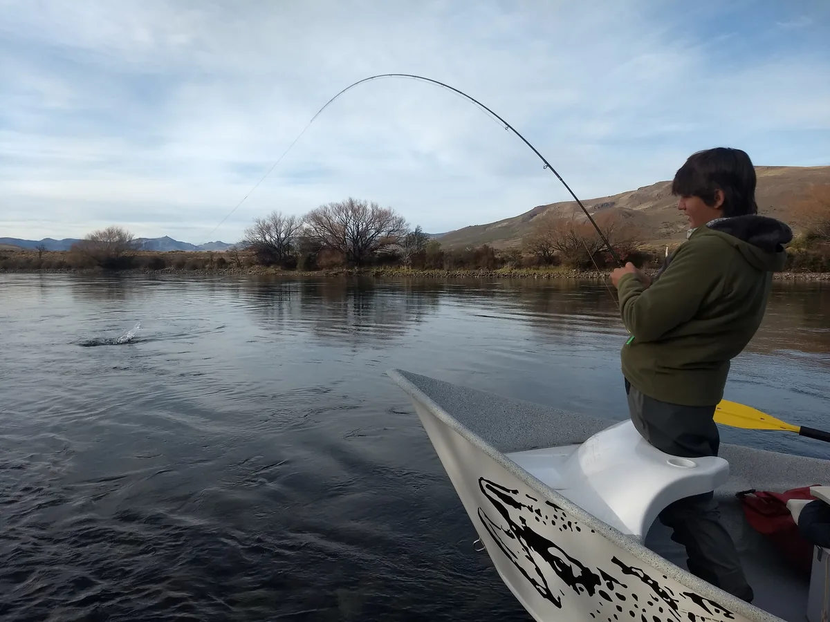 Angler playing a fish with a fly rod from a drift boat on a Patagonian river