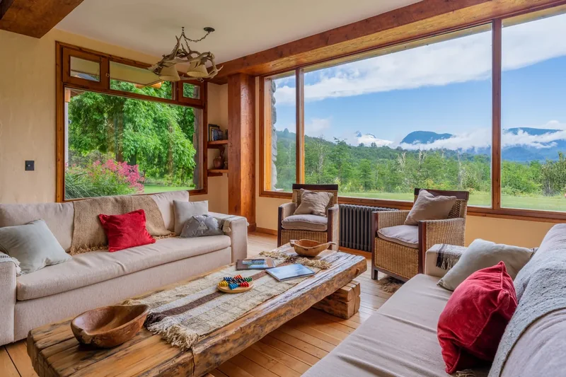 Living de un lodge de pesca con sillones, vigas de madera y grandes ventanas hacia el paisaje patagónico