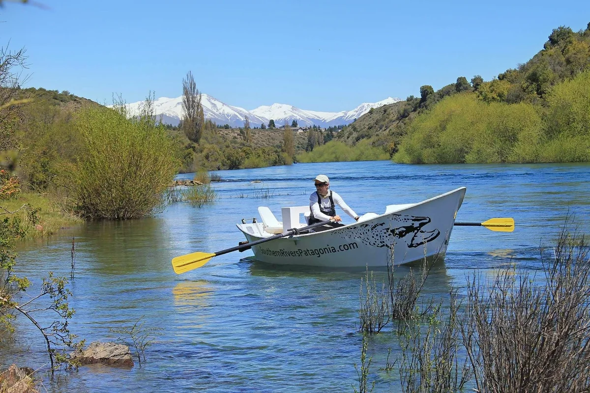 Guía remando un bote de pesca junto a una costa boscosa en Patagonia