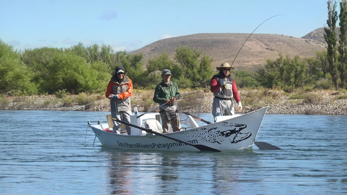 Two anglers and their guide in a drift boat on the Collón Cura River during a fly fishing trip in Patagonia