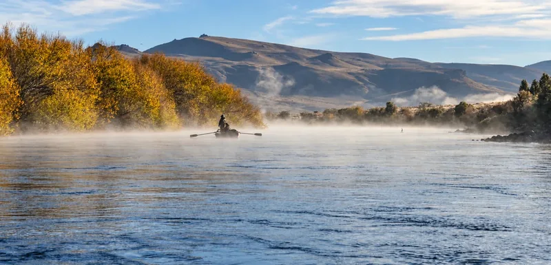 Bruma de la mañana sobre el río Limay, con árboles y cerros reflejados en el agua