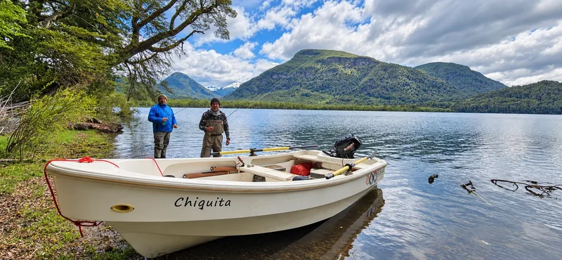 Fishing boat beside the wooded shore of Roca Lake with mountains in the background