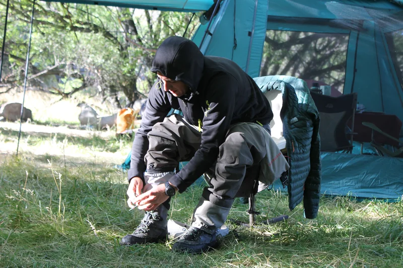 Pescador preparando las botas junto a una carpa en un campamento de pesca