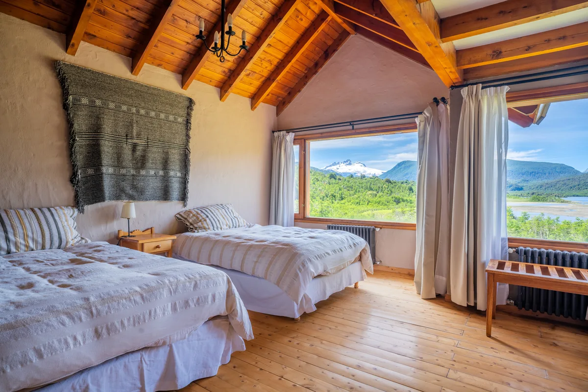 Fishing lodge bedroom with twin beds and views of the forest and snow-capped mountains in Patagonia