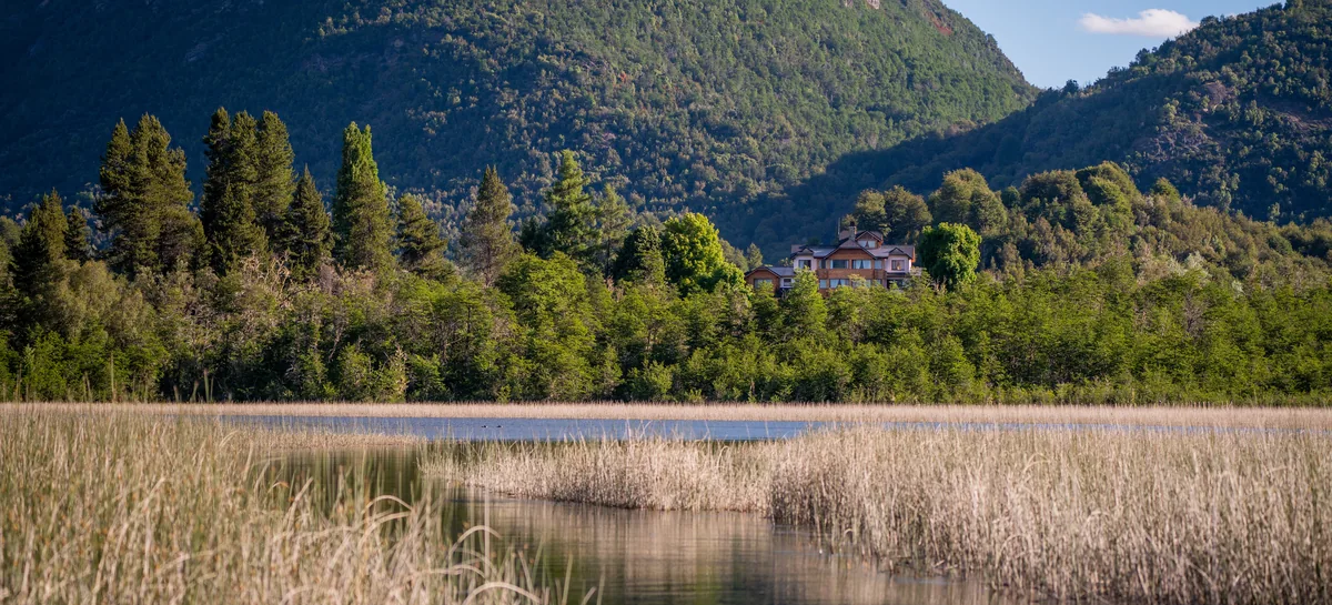 Rio Manso Fishing lodge nestled among forests and mountains beside a reed-lined Hess lake in Patagonia