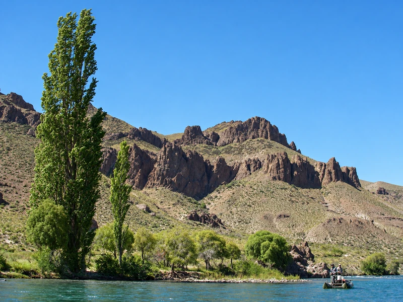 Fishing raft on the Caleufu River beneath poplar trees and rocky cliffs in Patagonia.