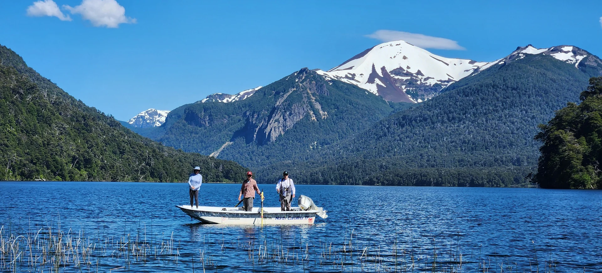 Fishing boat on a clear Patagonia lake beneath snow-capped Andes mountains