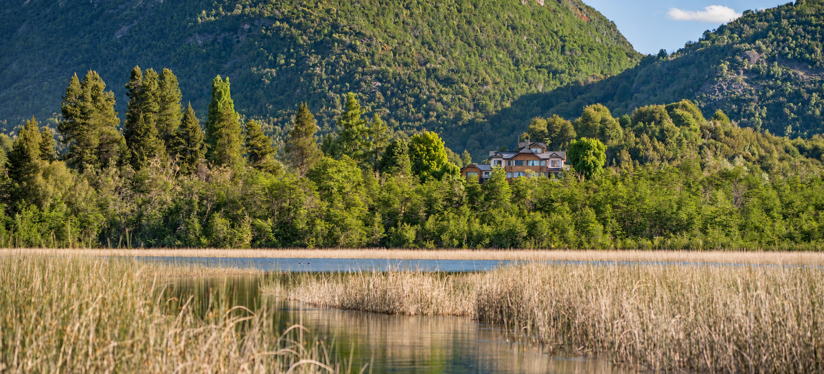 Río Manso Lodge surrounded by forest and mountains above the reed beds of Lake Hess, near Bariloche, Patagonia.