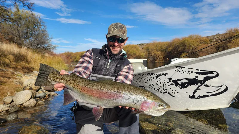 Angler holding a large rainbow trout beside a drift boat on the Limay River, Patagonia