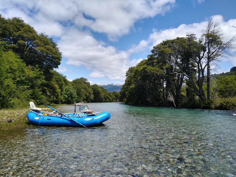 Fishing raft beside the clear waters of the Manso River, surrounded by native forest in Patagonia