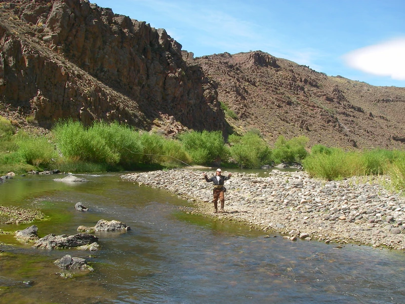 Angler fly fishing beside rocky cliffs on the Pichi Leufú River near Bariloche, Patagonia.