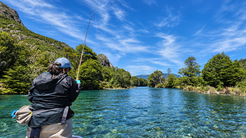 Pescador con la caña de mosca curvada en las aguas transparentes del río Manso, entre bosque nativo y montañas de la Patagonia
