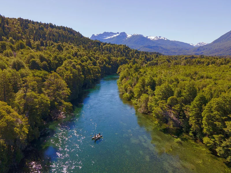 Aerial view of anglers floating the Manso River through native forest with the Andes in the background