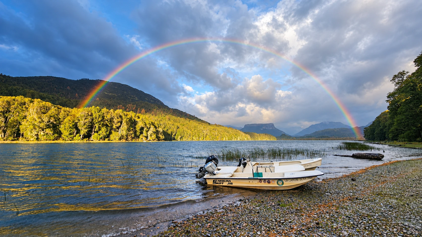 Rainbow over Lake Roca, with fishing boats by the shore and Patagonia’s mountains in the background.